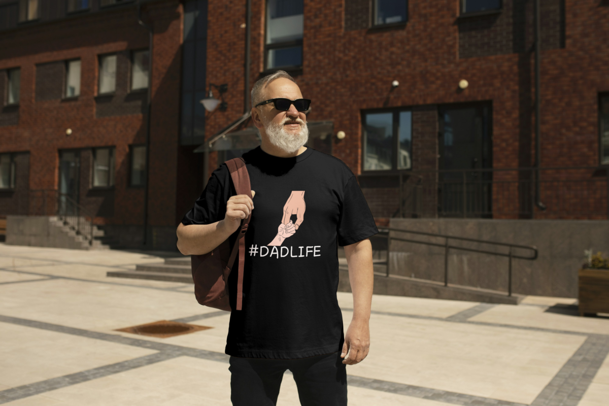 Man wearing an oversized black t-shirt with "#DadLife" and a design of a kid's hand shaking with his dad's hand by Attire Dot